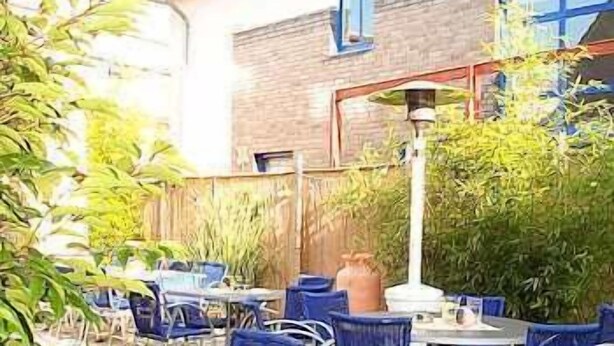An outdoor patio area with blue chairs and tables, surrounded by greenery and a brick wall. - Hotel Veltrup (Laer)