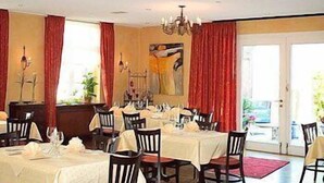 A dining area with tables set for a meal, red curtains, and a chandelier. - Hotel Veltrup (Laer)