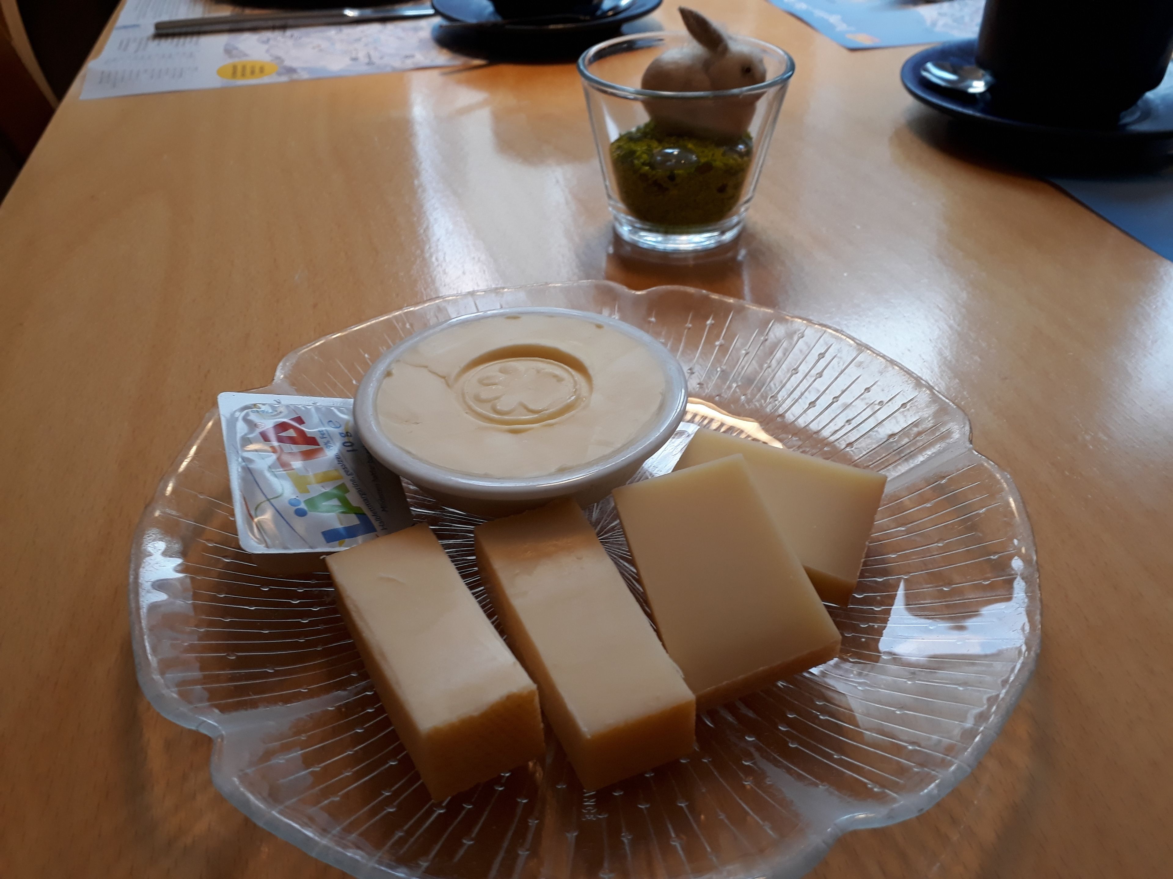 A clear glass plate with a bowl of soup, a packet of snacks, and several rectangular food items on a wooden table.