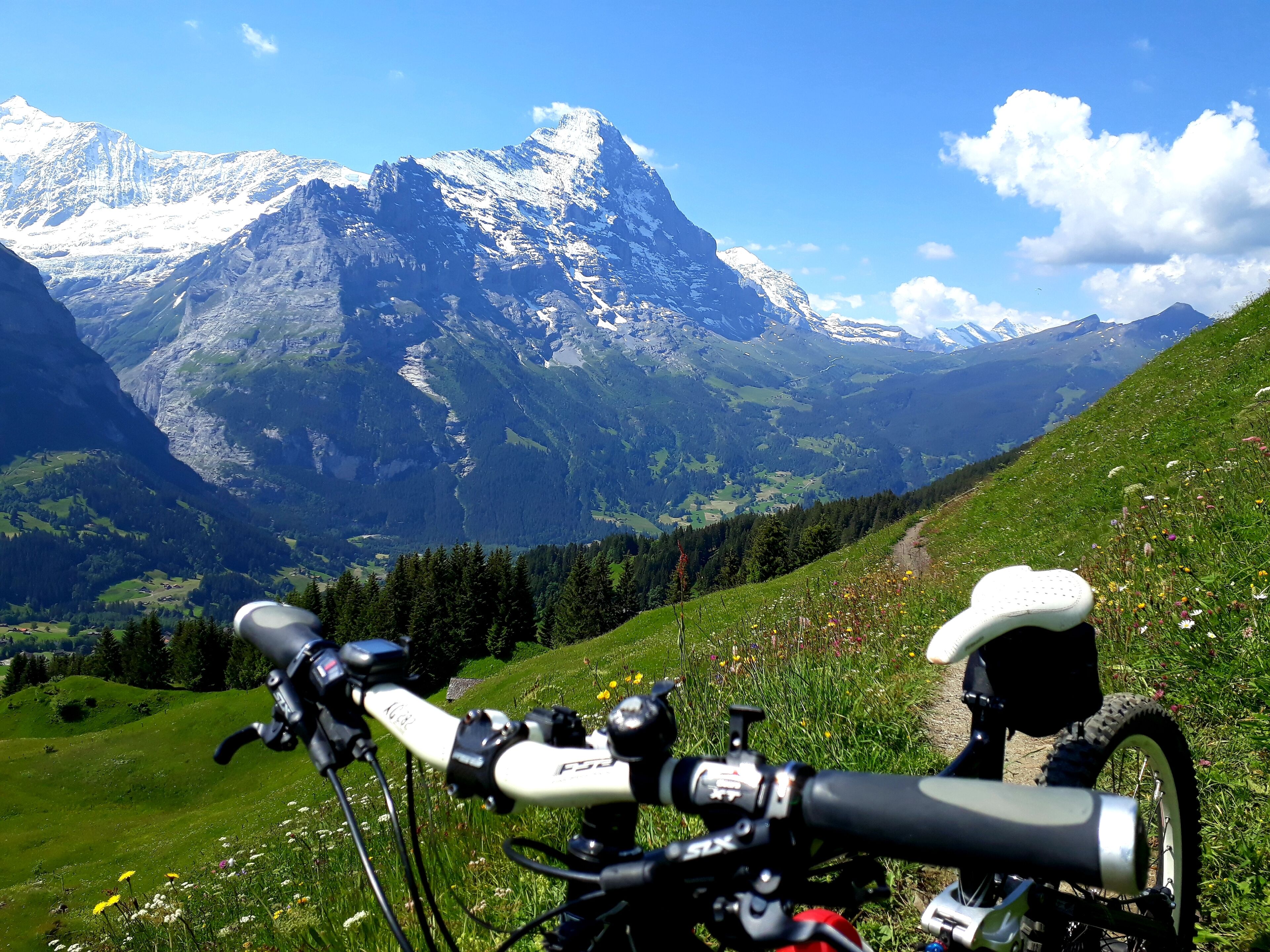 A bicycle with a camera mounted on it, positioned on a grassy hill with a mountain range in the background.