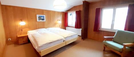 Una habitación con cama, una silla, una ventana con cortinas e iluminación en la pared.