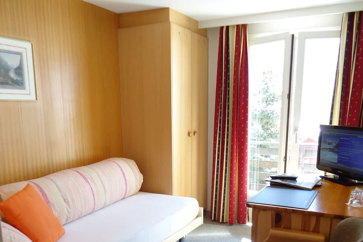 Una habitación de hotel con cama, escritorio con computadora, una silla y ventana con cortinas.