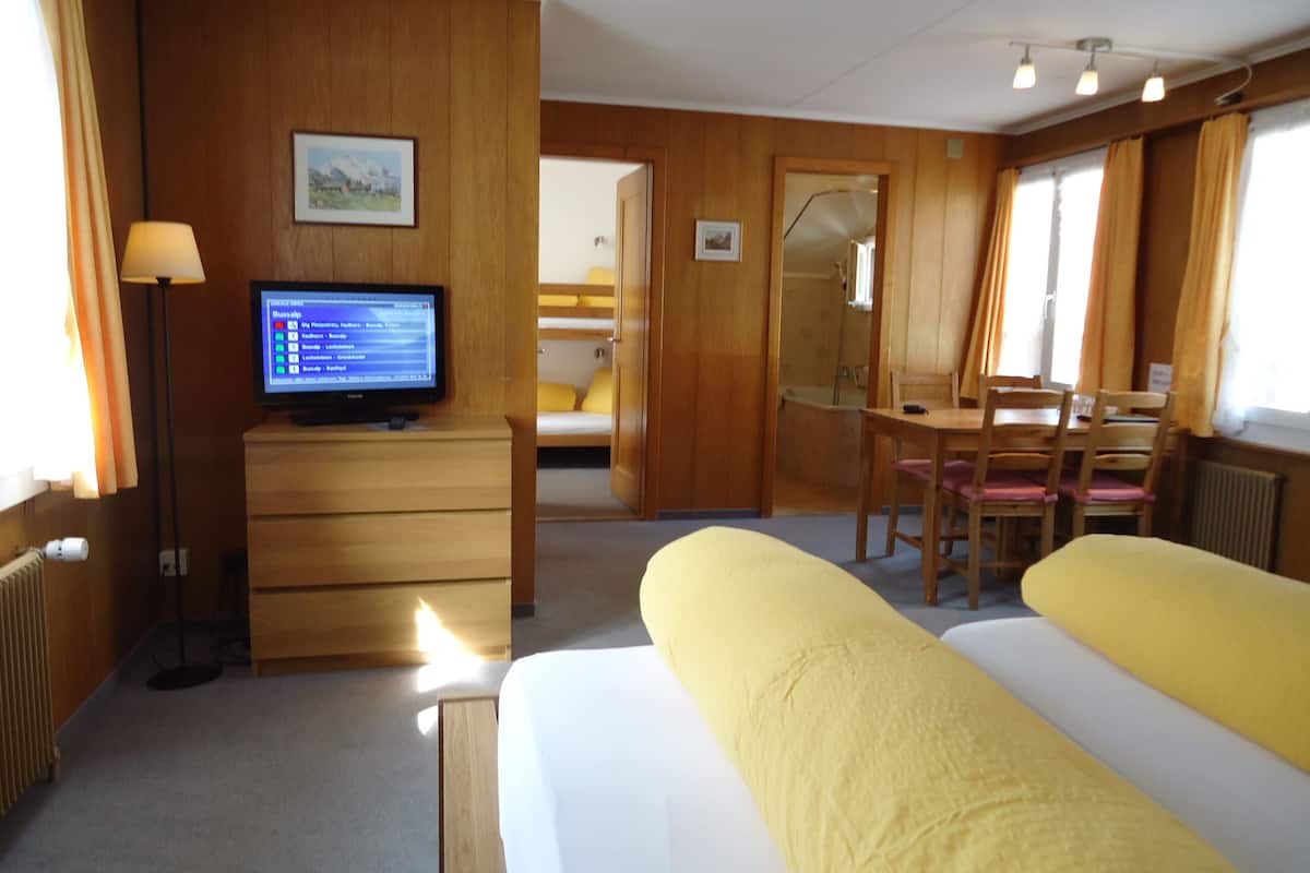 Habitación de hotel con cama, escritorio con computadora, silla, mesita y ventana con cortinas.