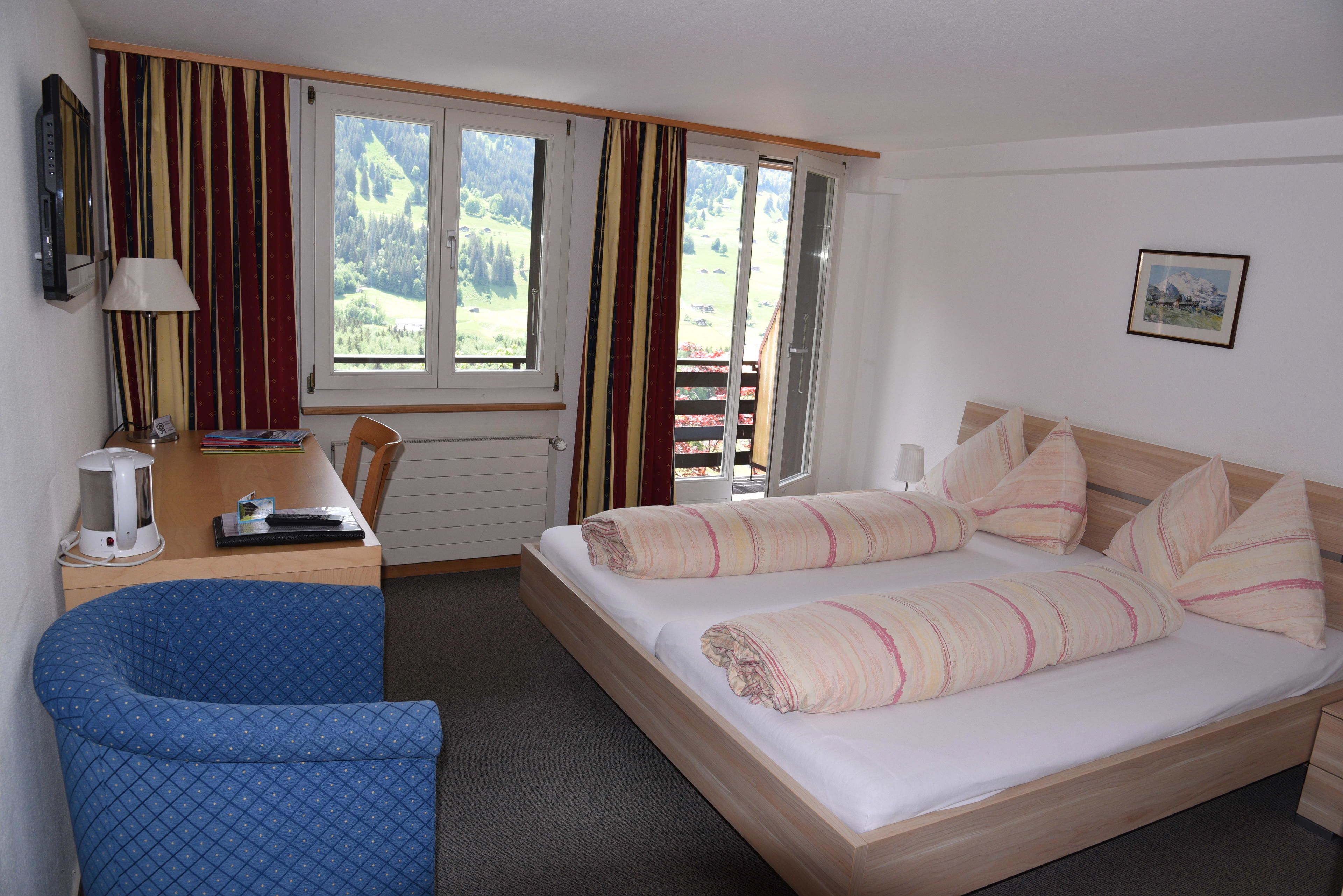 Une chambre à coucher avec un lit, un bureau, une chaise, une fenêtre avec des rideaux et un tableau au mur.
