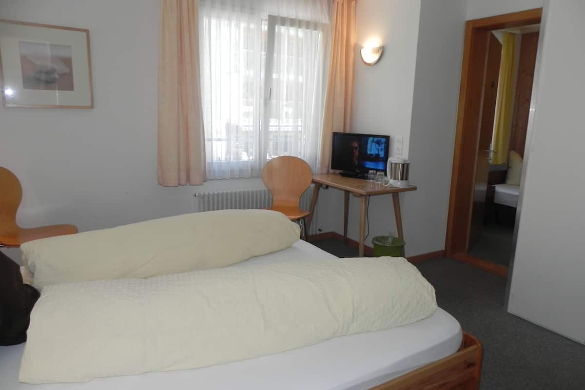 Una habitación de hotel con cama, una silla, televisor y una mesita con control remoto.