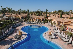 A large swimming pool with multiple lanes, surrounded by lounge chairs and umbrellas, with buildings and palm trees in the background. - Maspalomas Resort by Dunas (San Bartolomé de Tirajana)