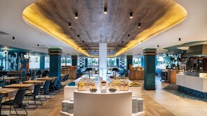 A modern restaurant with a central buffet, wooden ceiling, and large windows. - Maspalomas Resort by Dunas (San Bartolomé de Tirajana)