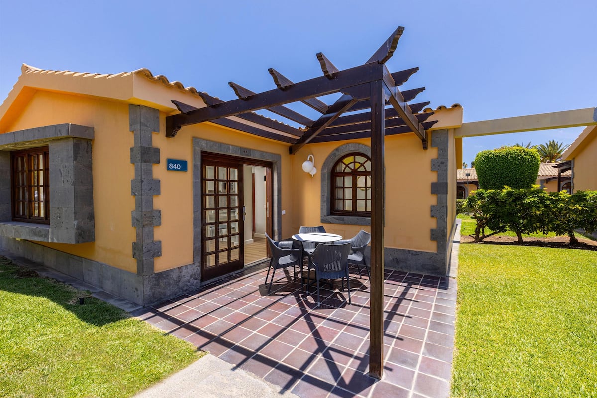 A house with a patio, a number 840 sign, a pergola, and a well-maintained lawn.