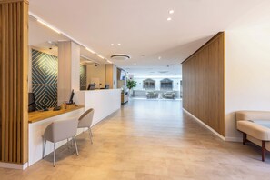 A modern reception area with a wooden desk, two chairs, and a seating area with a bench. - Maspalomas Resort by Dunas (San Bartolomé de Tirajana)