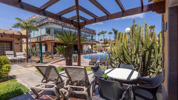 A poolside area with lounge chairs and a table, surrounded by cacti and palm trees.