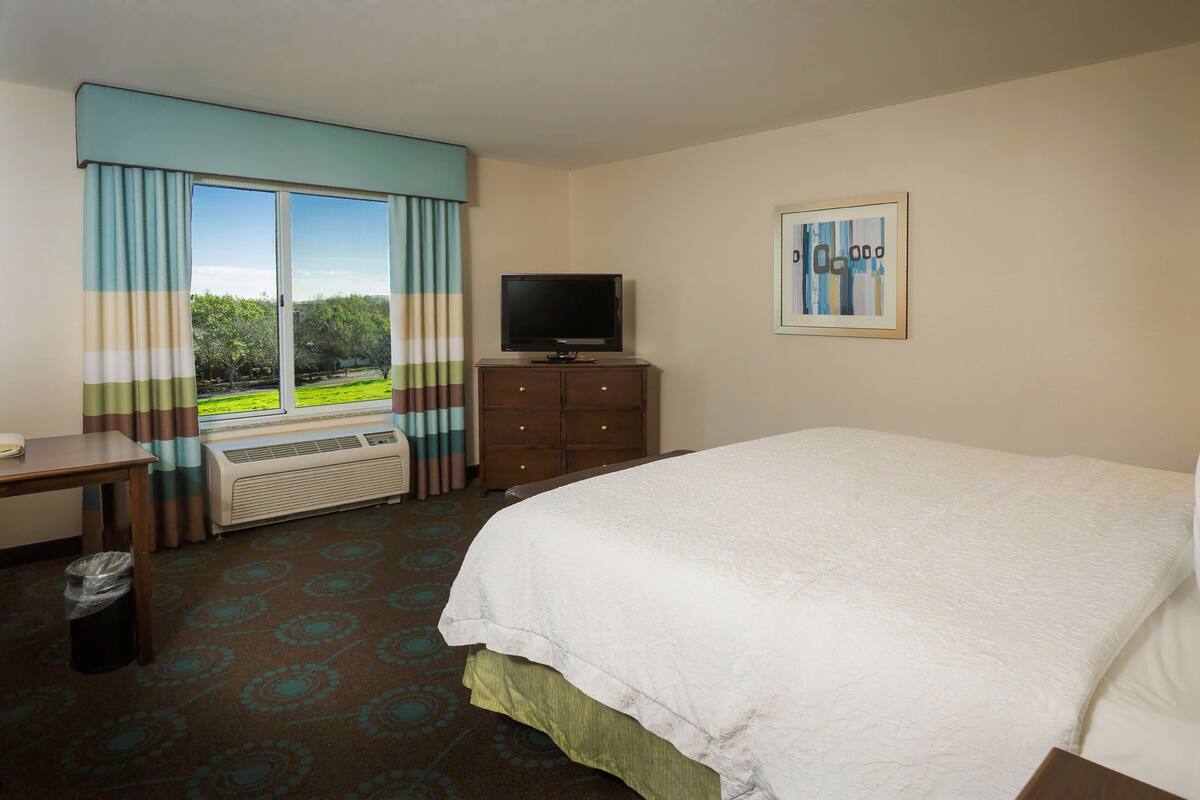 A hotel room with a bed, a television, a desk, and a window with curtains.