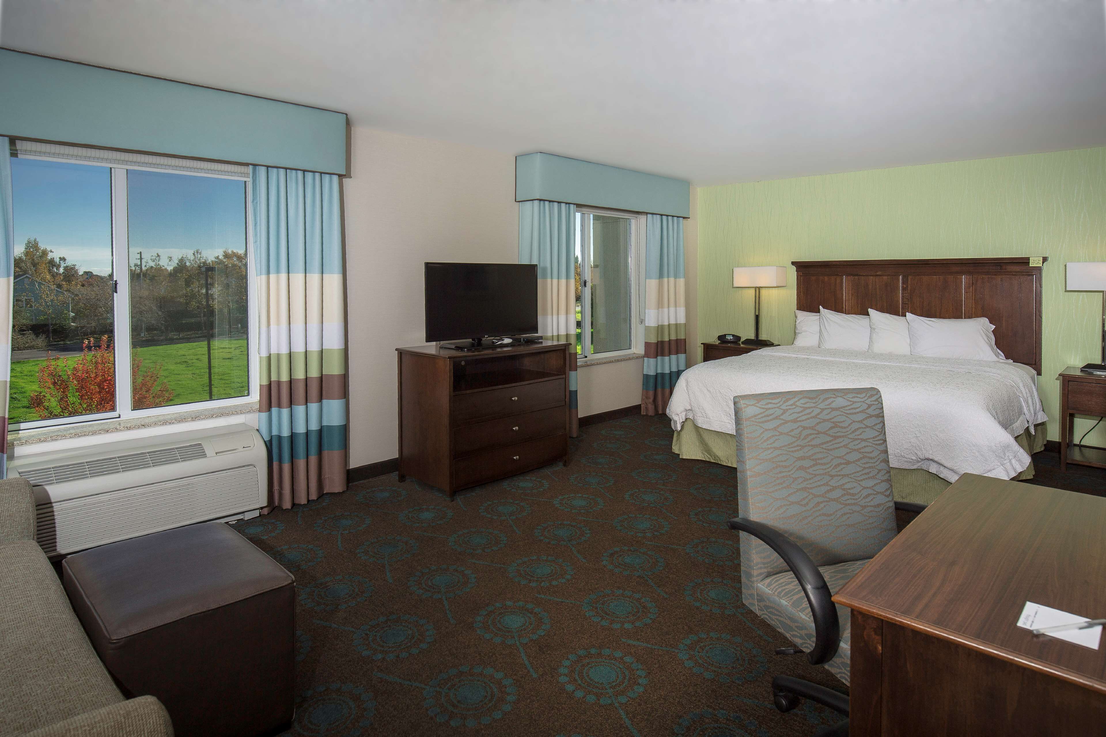 A hotel room with a large bed, a desk, a chair, a television, and a window with curtains.