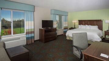 A hotel room with a large bed, a desk, a chair, a television, and a window with curtains.