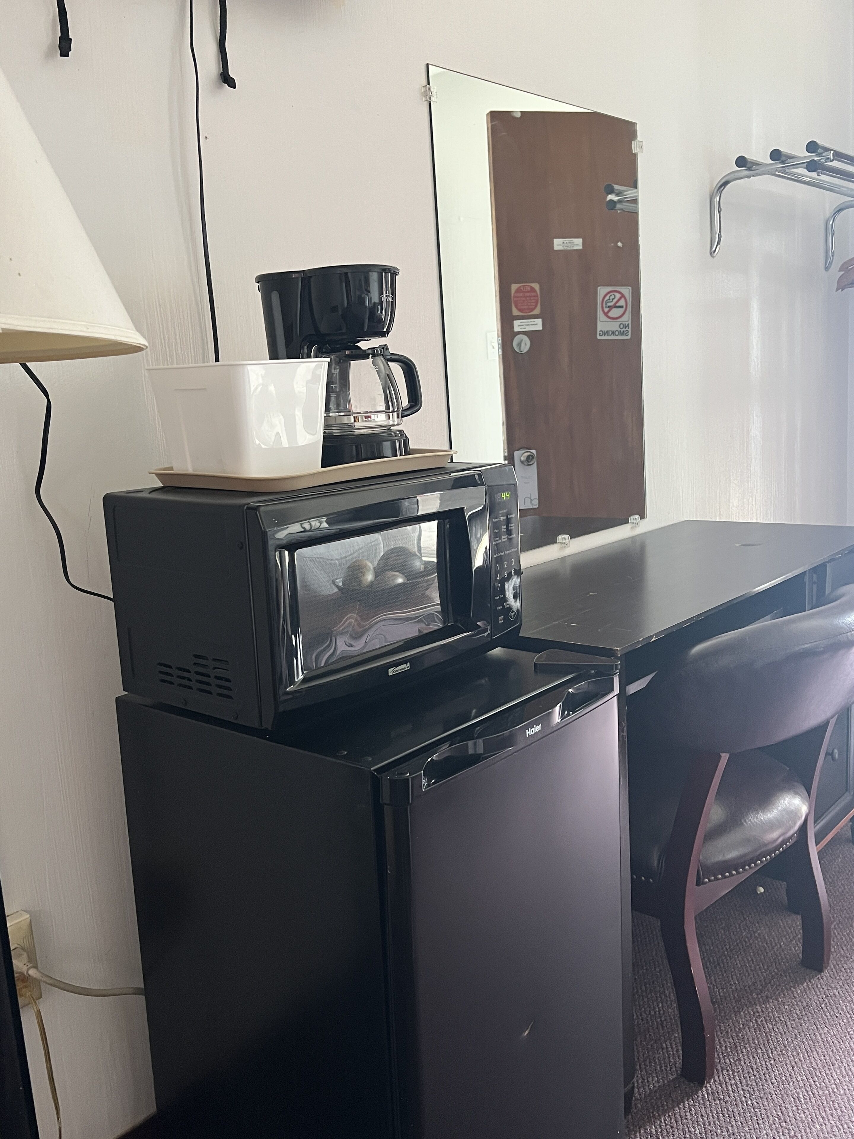 A compact kitchenette with a microwave, coffee maker, and a white cup on the counter.
