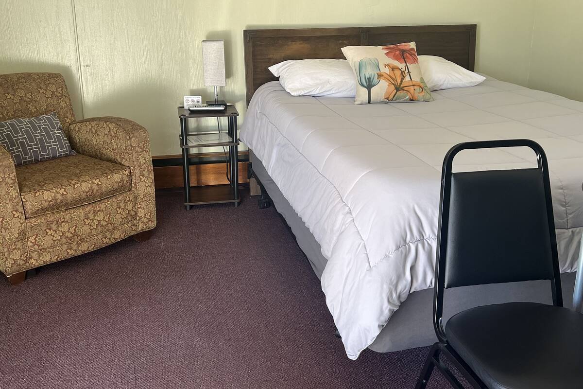 A hotel room with a bed, a chair, a nightstand, and a lamp.