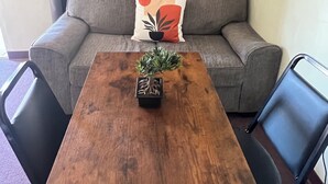 A room with a wooden table, two black chairs, a grey sofa with a decorative pillow, and a small potted plant on the table.