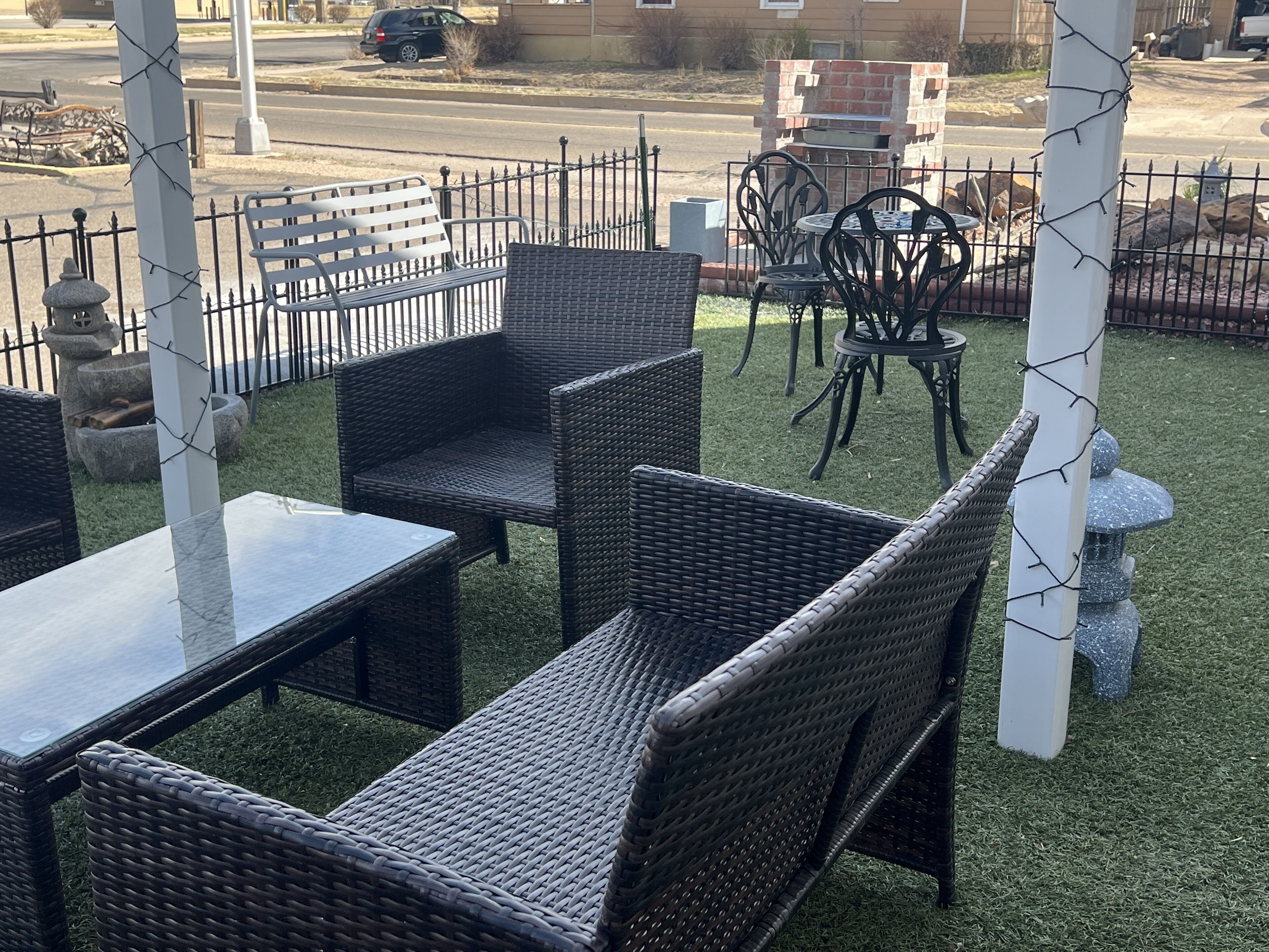 Outdoor wicker furniture with a glass table, a stone lantern, and a brick oven.