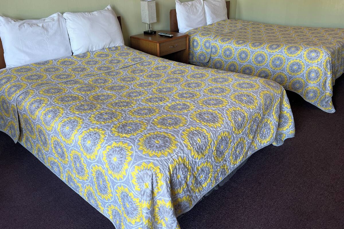 Two single beds with patterned bedding, a nightstand with a lamp, and a wooden headboard.