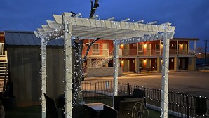 A covered outdoor seating area with string lights, a statue, and a building in the background.