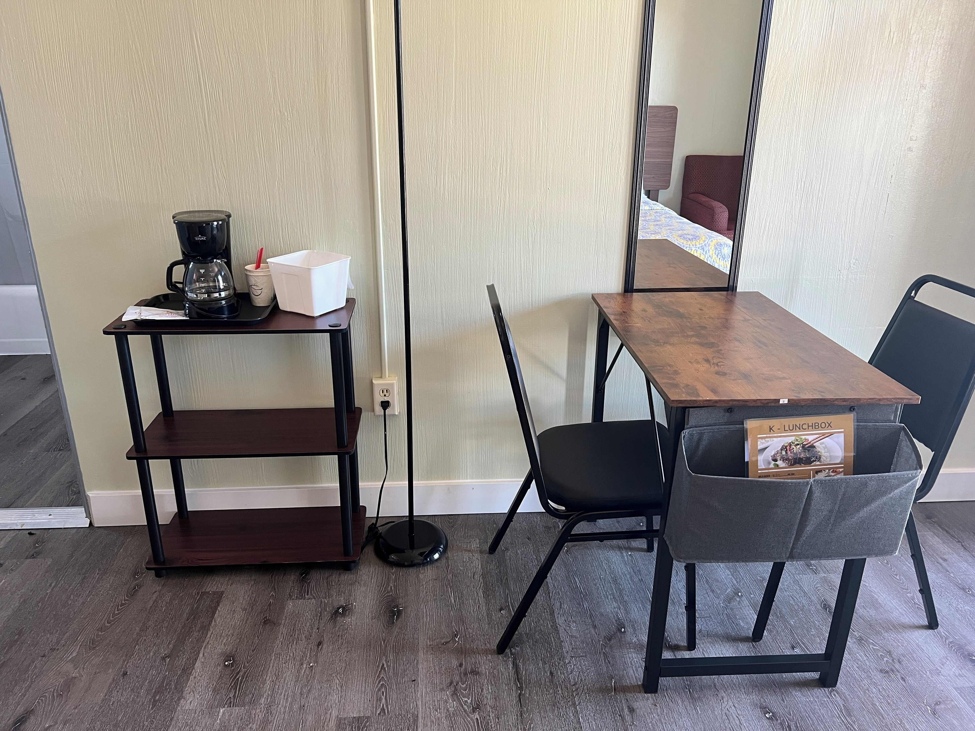 A small dining area with a wooden table, black chairs, a coffee machine, and a lunchbox on the table.
