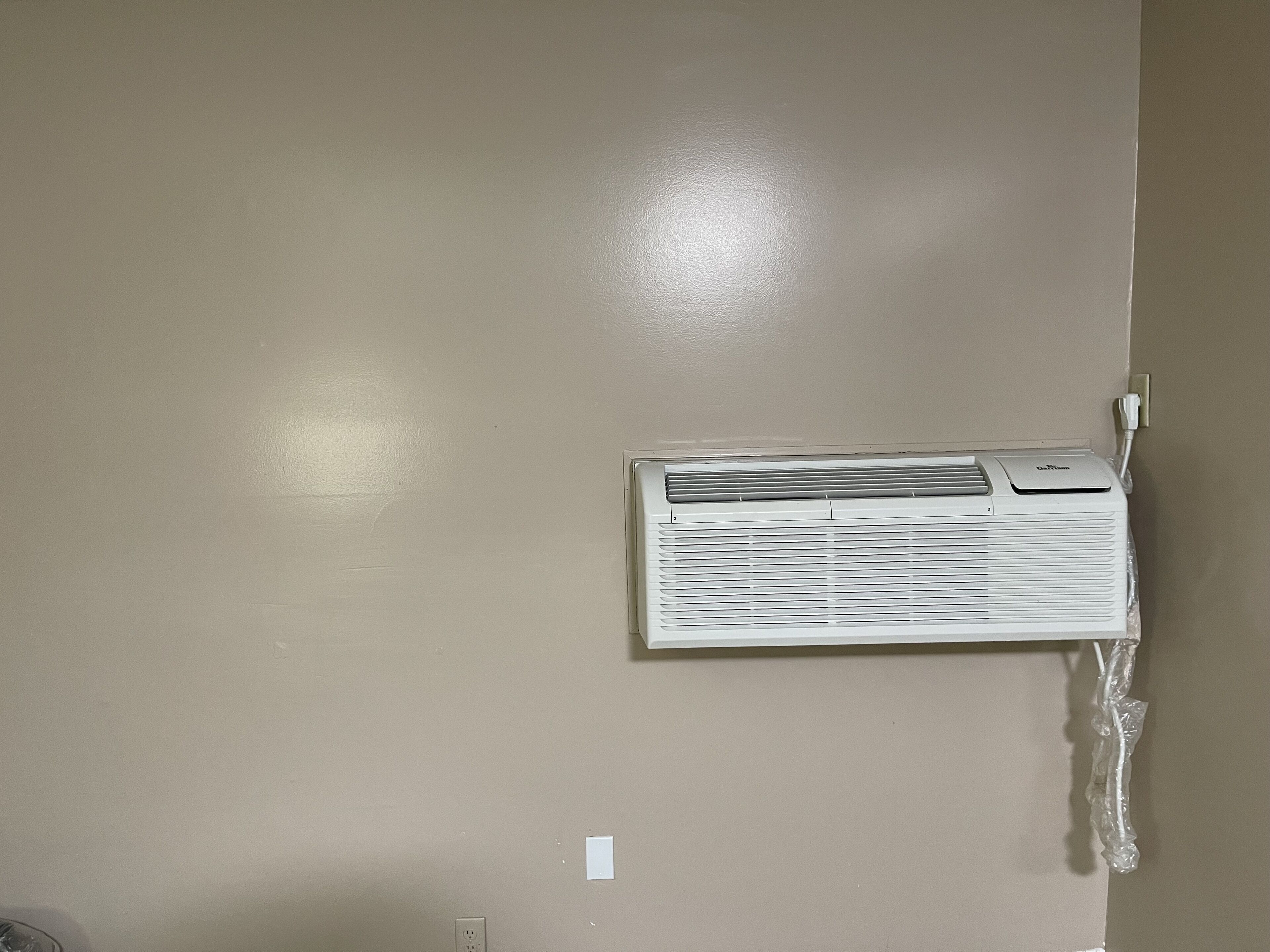 Un equipo de aire acondicionado blanco montado en una pared color beige, con un enchufe y una toma de corriente a la vista.