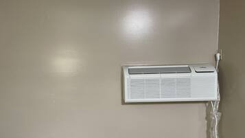 Un equipo de aire acondicionado blanco montado en una pared color beige, con un enchufe y una toma de corriente a la vista.