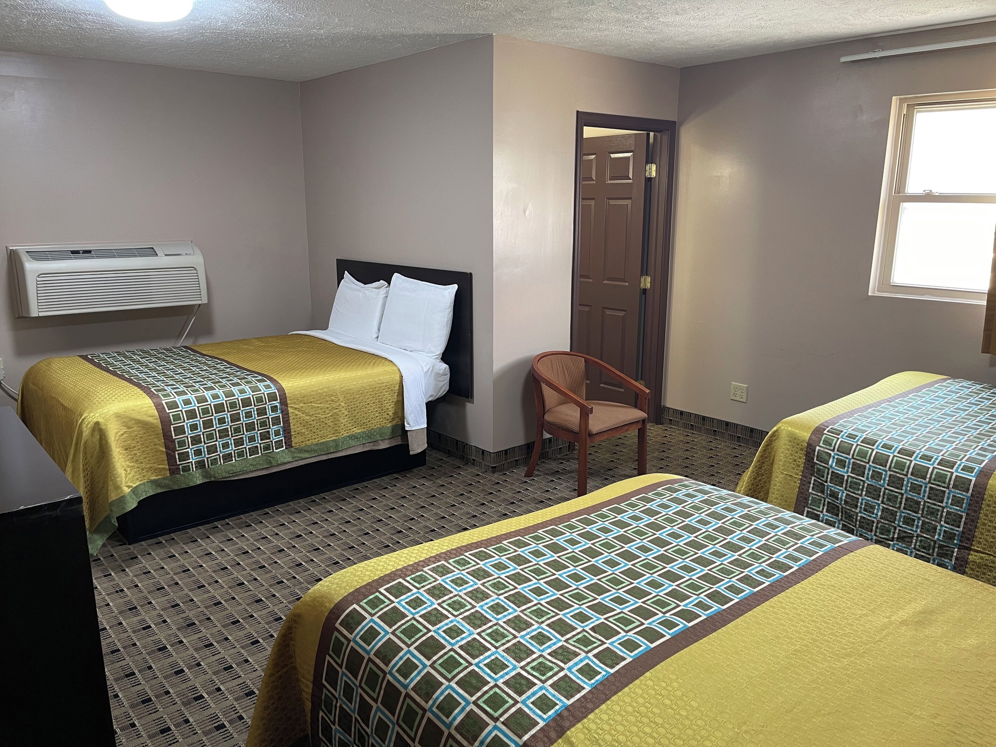 Habitación de hotel con dos camas, una silla, un equipo de aire acondicionado y una puerta.