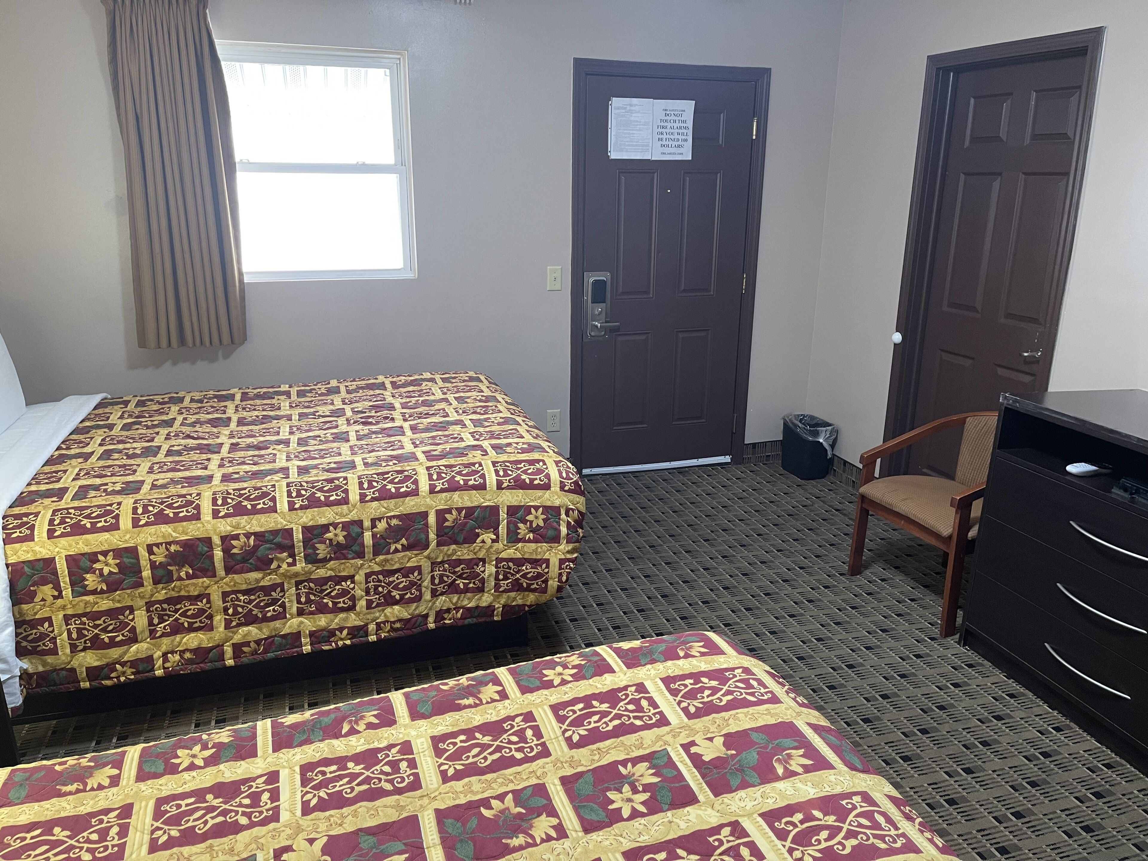 A hotel room with a large bed, a smaller bed, a desk, a chair, and a door with a notice.