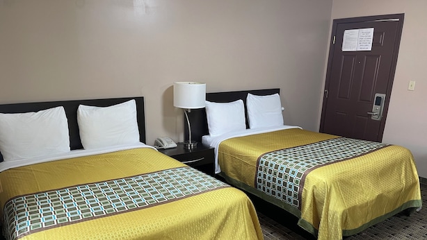 Two double beds with yellow and green patterned bedspreads, a bedside table with a lamp, and a door with a fire safety sign. - Economy Inn And Suites Ashtabula (Ashtabula)