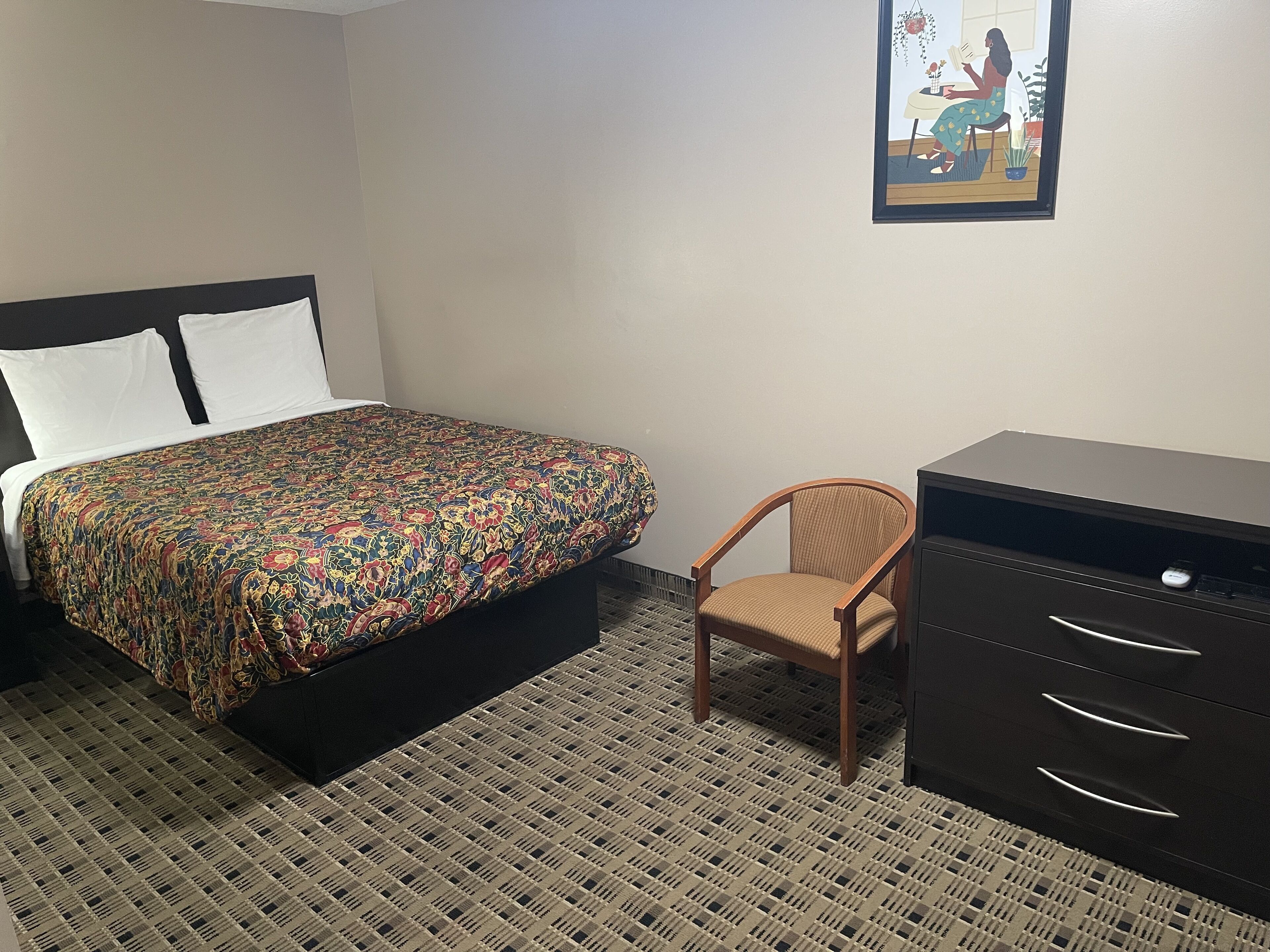 A hotel room with a bed, a chair, a desk, and a filing cabinet.