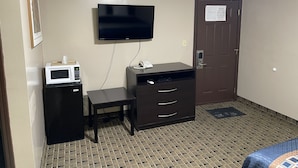 A hotel room with a flat-screen TV mounted on the wall, a small desk with a telephone, a microwave, and a dark-colored wardrobe with two drawers. - Economy Inn And Suites Ashtabula (Ashtabula)