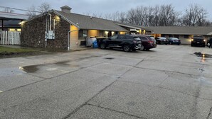 A motel with a stone exterior, a covered parking area, and several cars parked in front. - Economy Inn And Suites Ashtabula (Ashtabula)