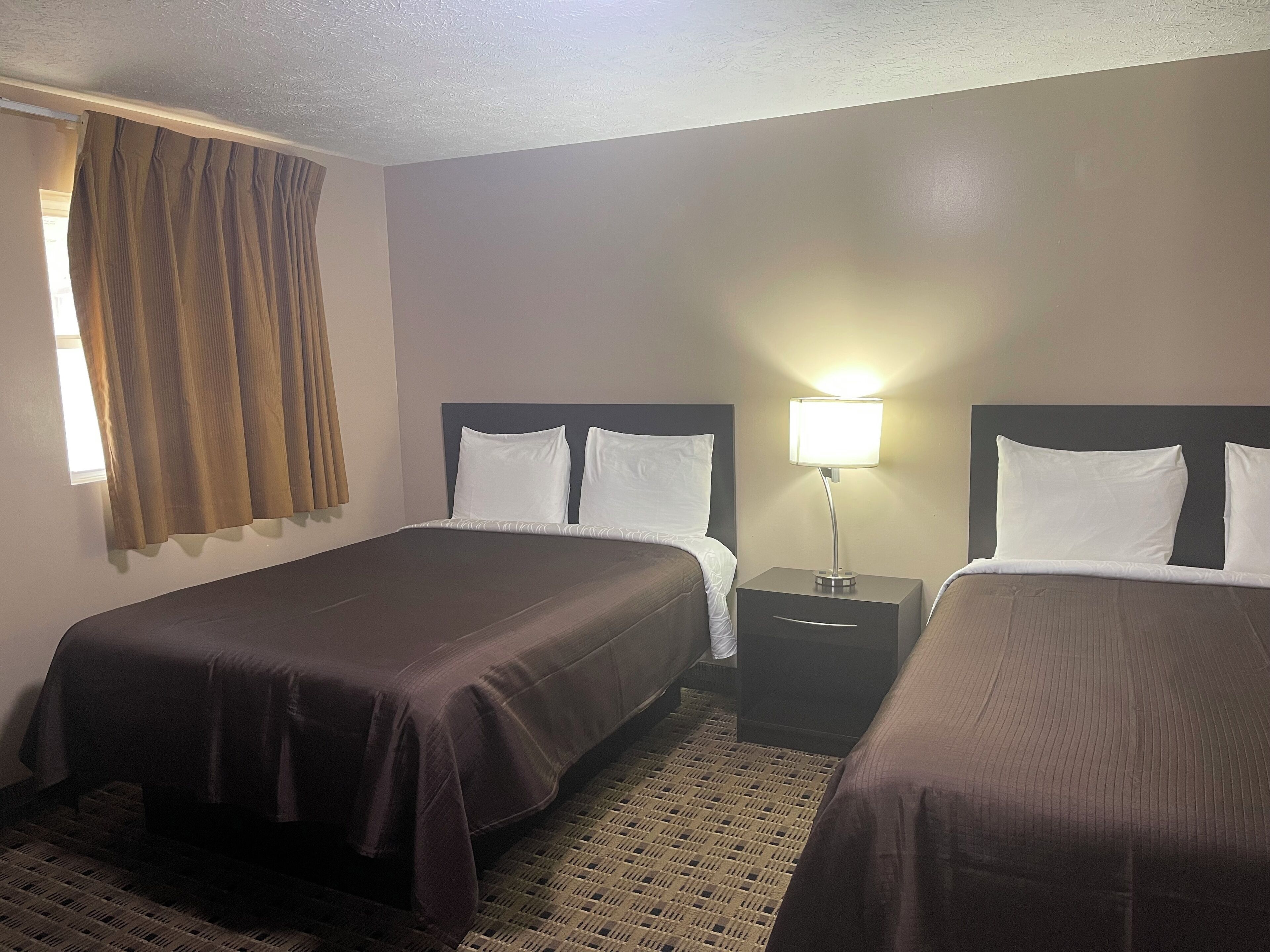 Une chambre d’hôtel avec deux lits, une table de chevet, une lampe et une fenêtre avec des rideaux.
