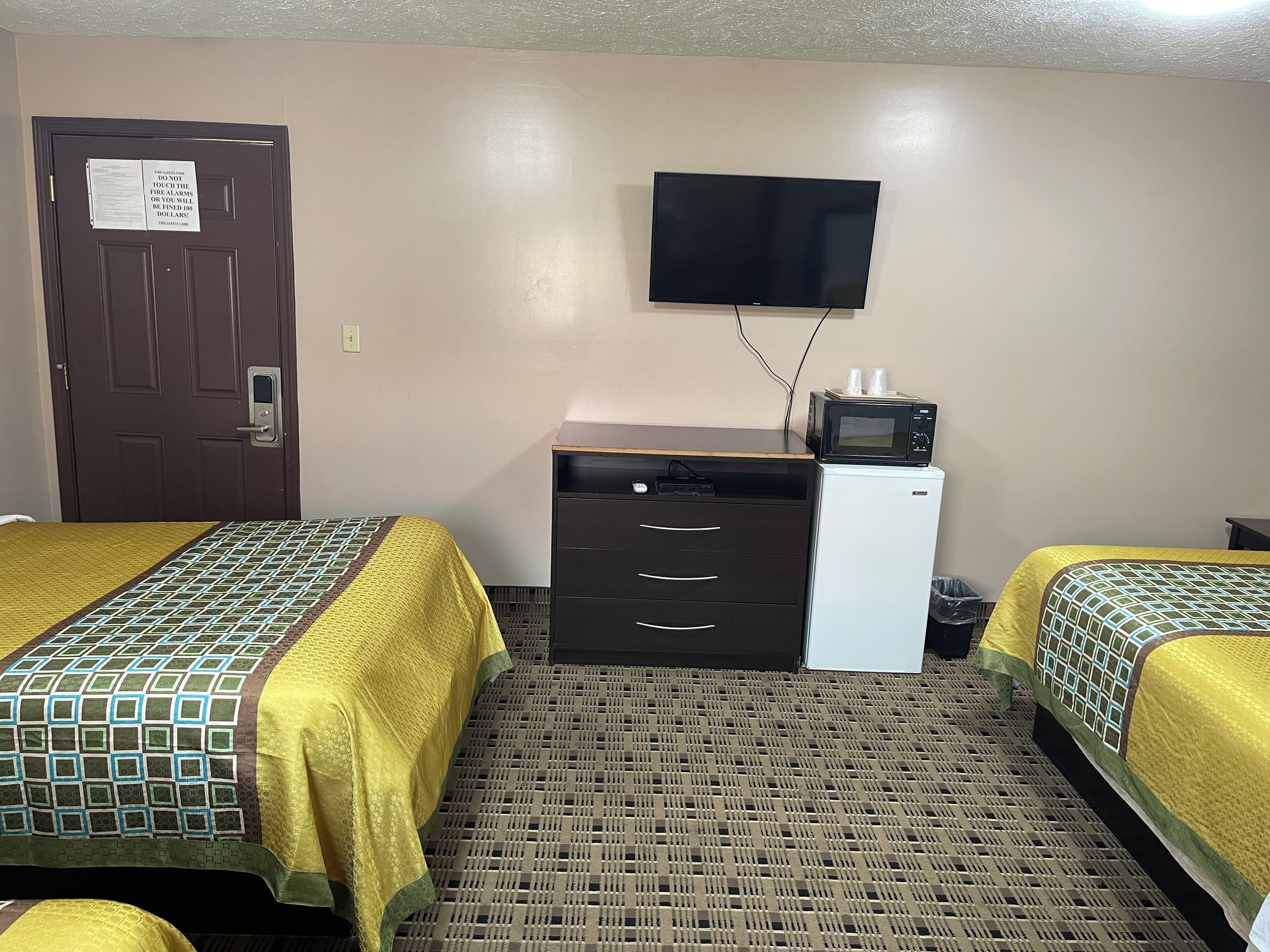 A hotel room with two beds, a desk with a microwave, a television, and a door with a safety notice.