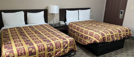 A hotel room with two beds, each with a patterned bedspread, a bedside table with a lamp, and a door with a security notice.