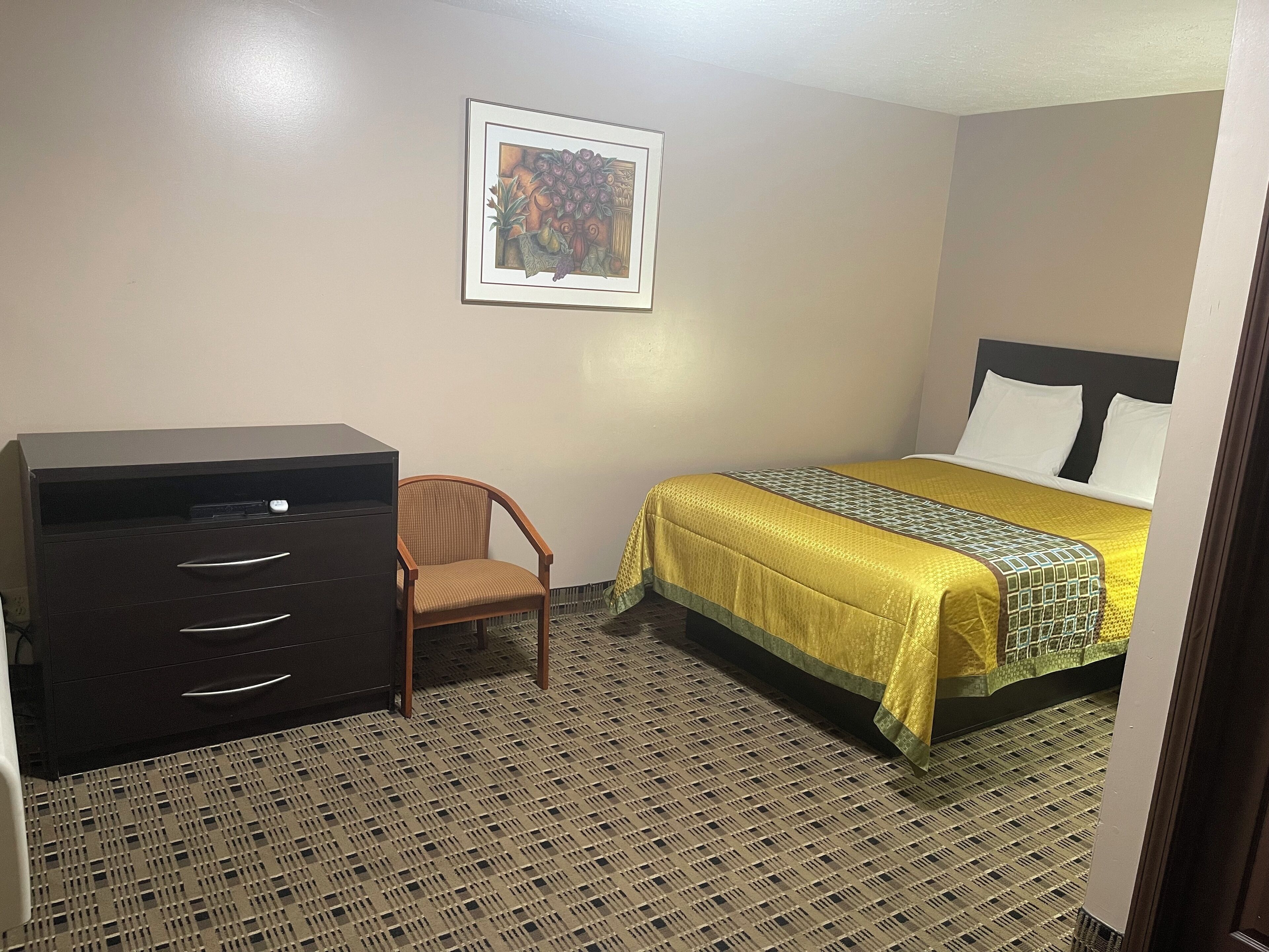 Una habitación de hotel con cama, escritorio, silla y un cuadro en la pared.