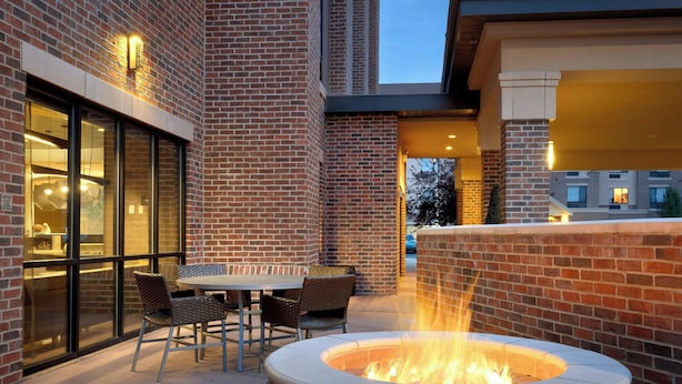 An outdoor patio with a brick fire pit, seating area, and a glass wall.