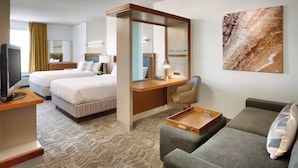 A hotel room with two beds, a desk, a chair, a sofa, and a television.