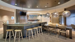 A modern bar area with a curved counter, wooden stools, and hanging pendant lights.