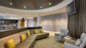 A modern lobby with a curved ceiling, a seating area with a sofa and armchairs, a bar area, and a flat-screen TV mounted on the wall.
