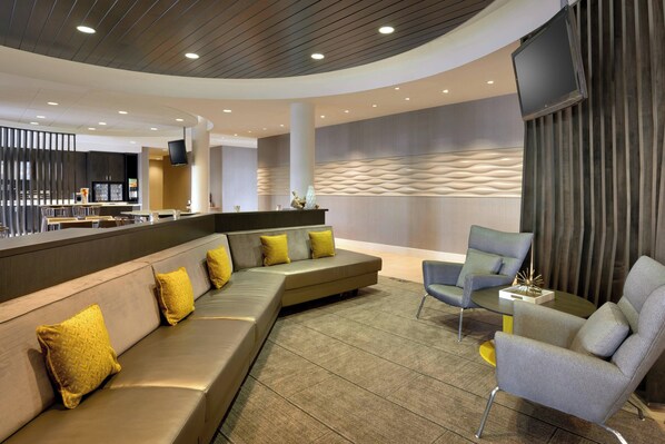 A modern lobby with a curved ceiling, a seating area with a sofa and armchairs, a bar area, and a flat-screen TV mounted on the wall. - SpringHill Suites by Marriott Vernal (Vernal)