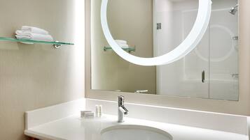 A modern bathroom with a large mirror, a sink, and a glass shelf holding towels.