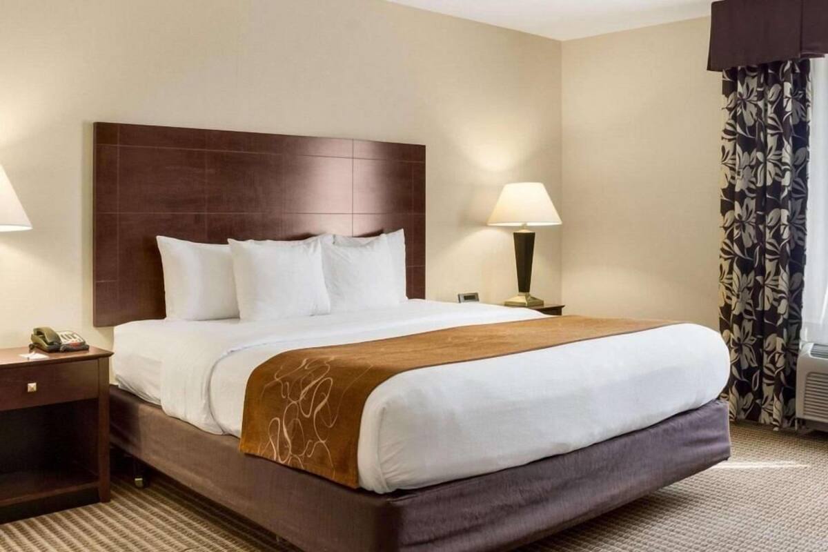 A hotel room with a large bed, two bedside tables, a nightstand, a lamp, and a window with curtains.