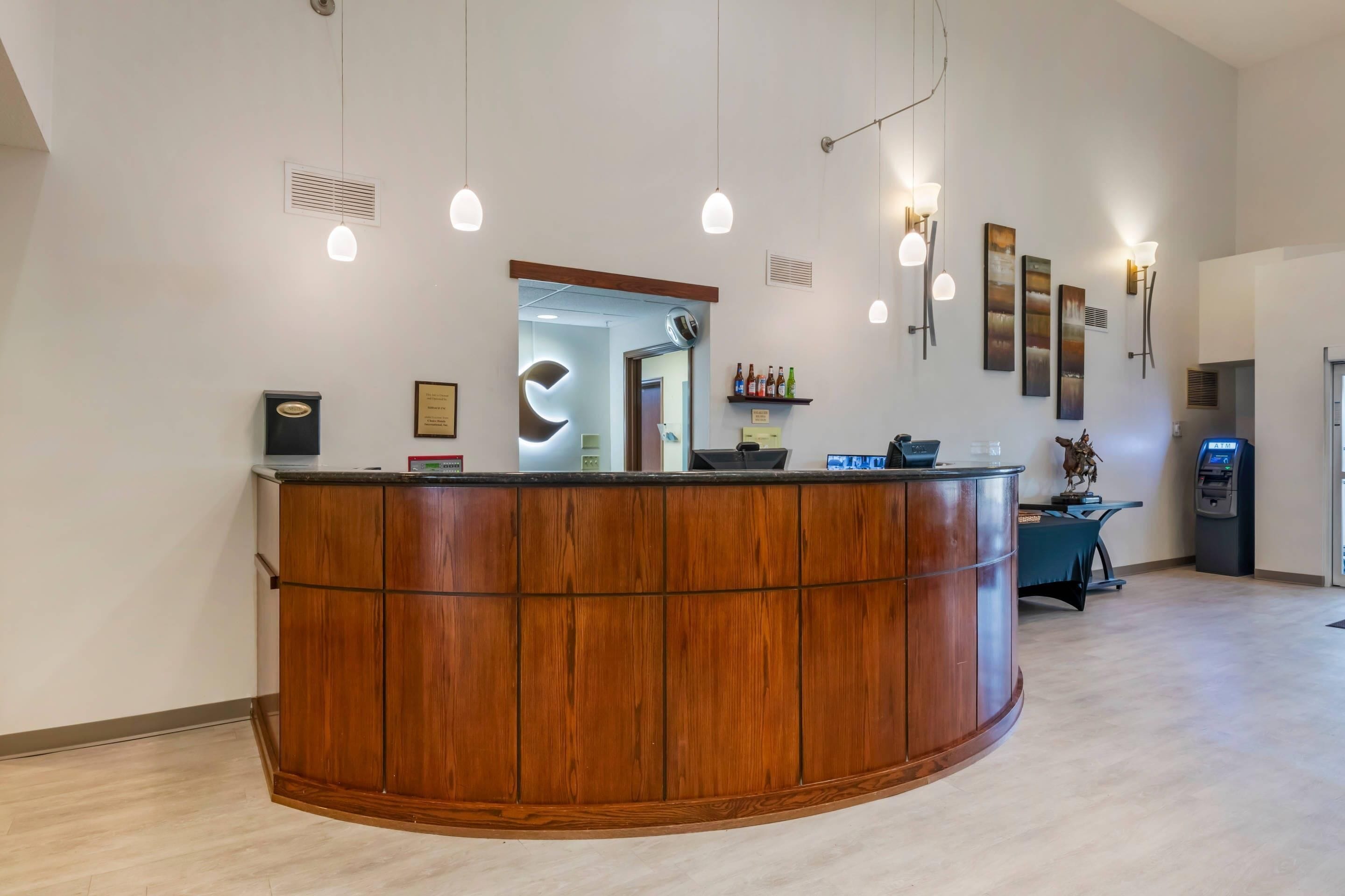 A reception desk with a wooden finish, a wall-mounted light fixture, and a digital kiosk.