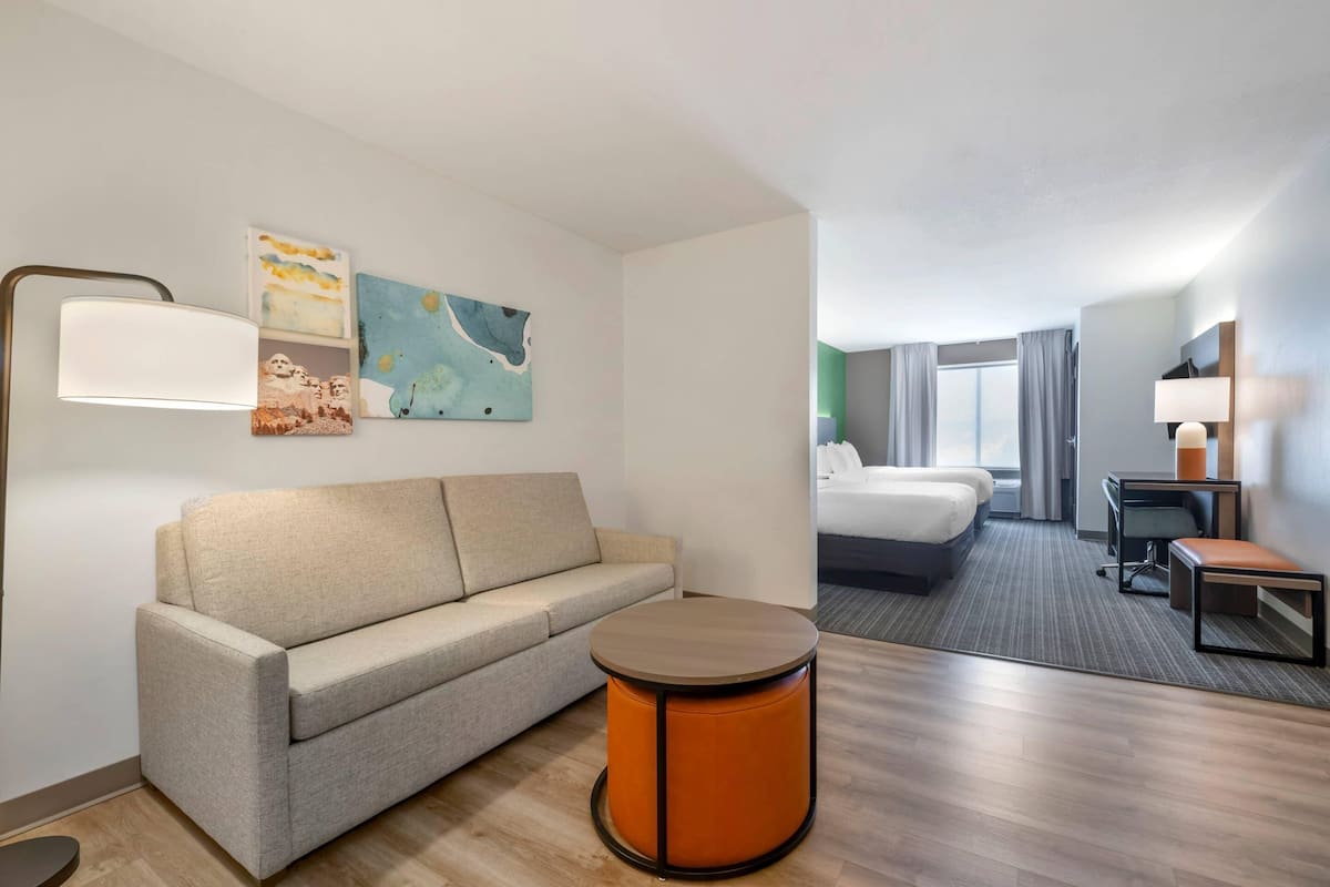 A hotel room with a sofa, a round table, a bed, a desk, and a chair.