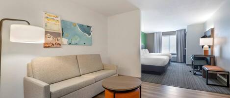 A hotel room with a sofa, a round table, a bed, a desk, and a chair.