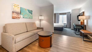 Ein Hotelzimmer mit einer Couch, einem runden Tisch, einem Schreibtisch, einem Stuhl, einem Fernseher und Bildern an der Wand.