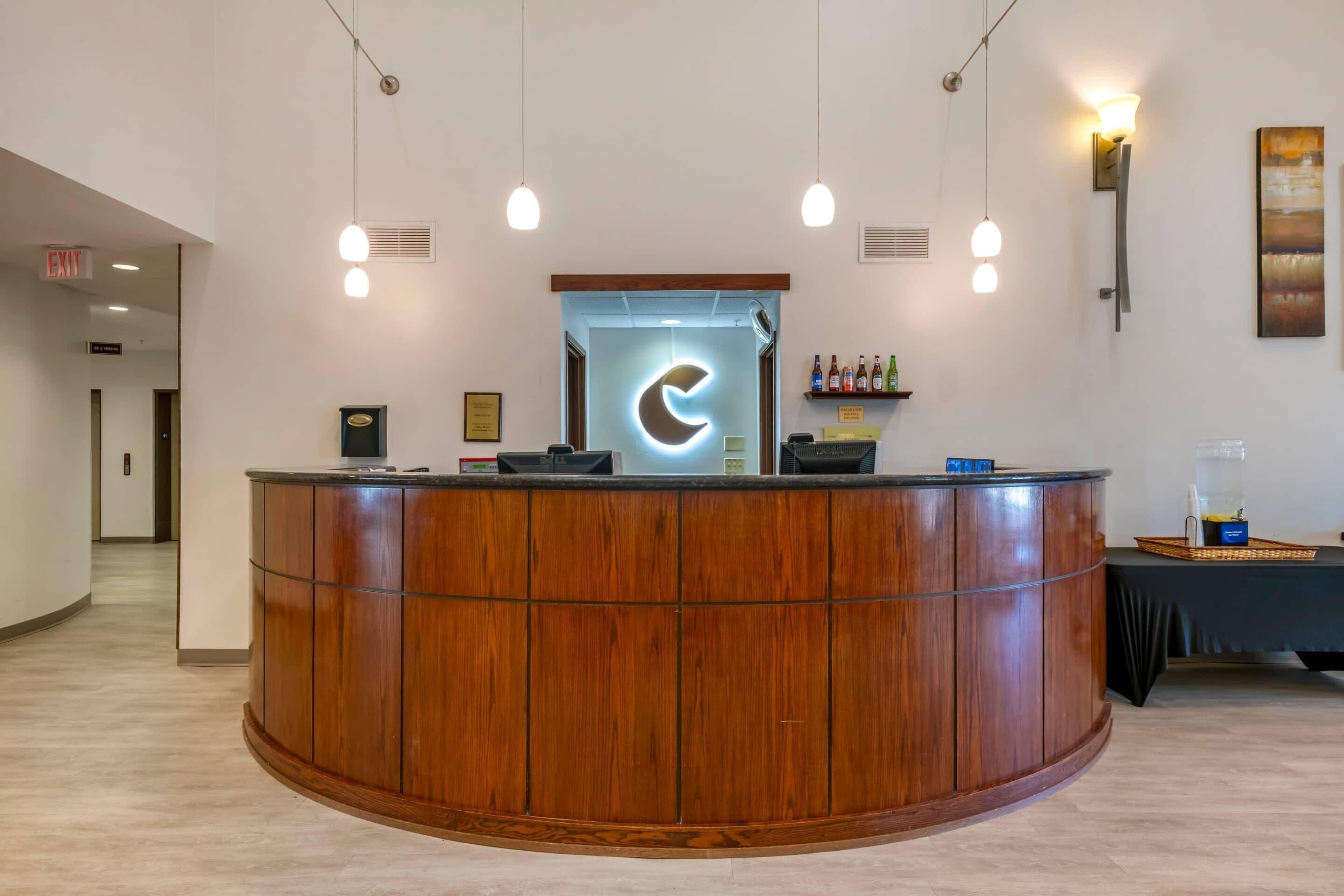 A reception desk with a logo, a wall-mounted shelf with bottles, and a framed certificate on the wall.