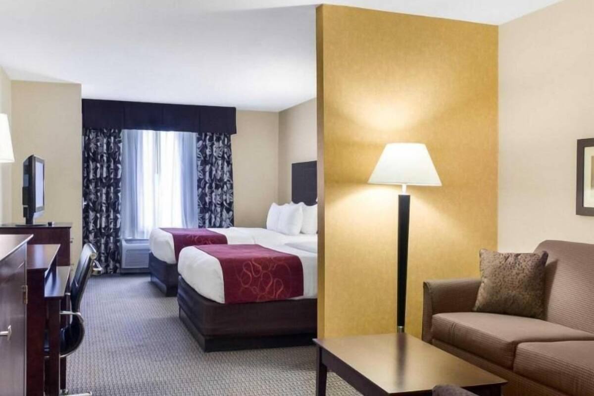 A hotel room with a bed, a desk, a chair, a sofa, a lamp, and a window with curtains.
