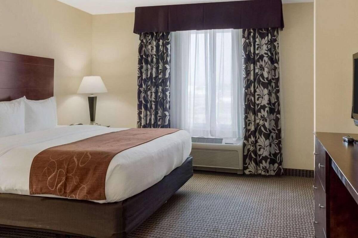 A hotel room with a bed, a bedside lamp, a window with curtains, a flat-screen TV, and a dresser.